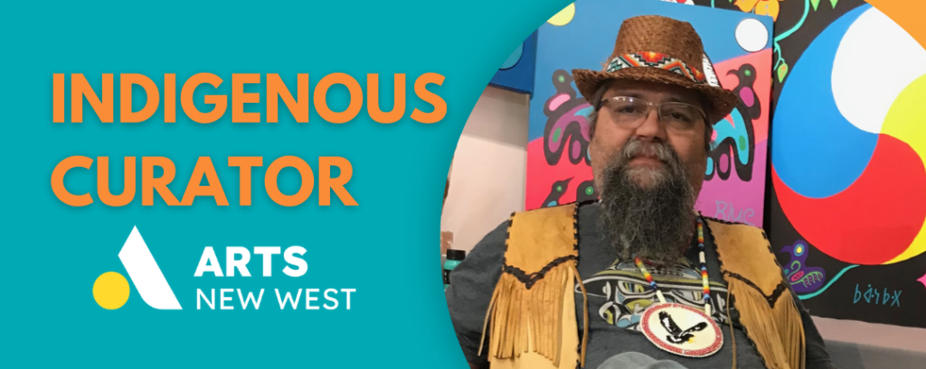 James sits on a chair in front of a collection of his artwork. He is a middle aged man with short dark hair and a grey and black beard. He wears a woven hat with colourful beadwork, a tan vest, a grey shirt and jeans.