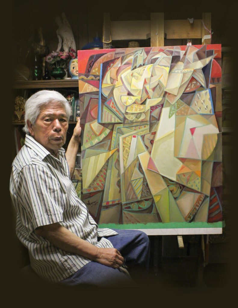 A self portrait photograph of the artist sitting next to one of his abstract pieces resting on an easel.
