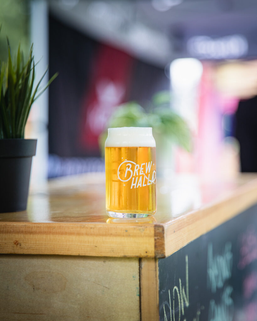 A full glass of beer sits on a wooden countertop surrounded by plants