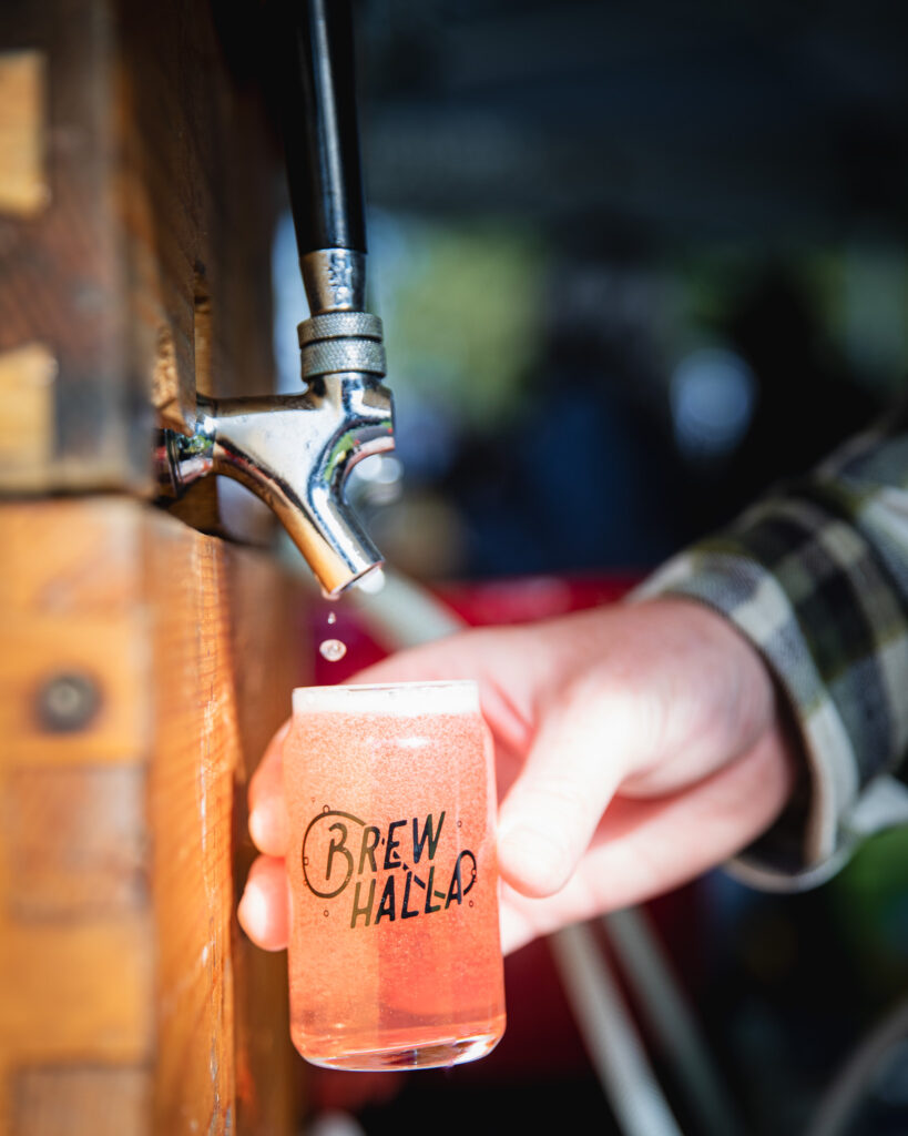 The last drops of pink cider fall from the tap of a wooden keg into a glass. 