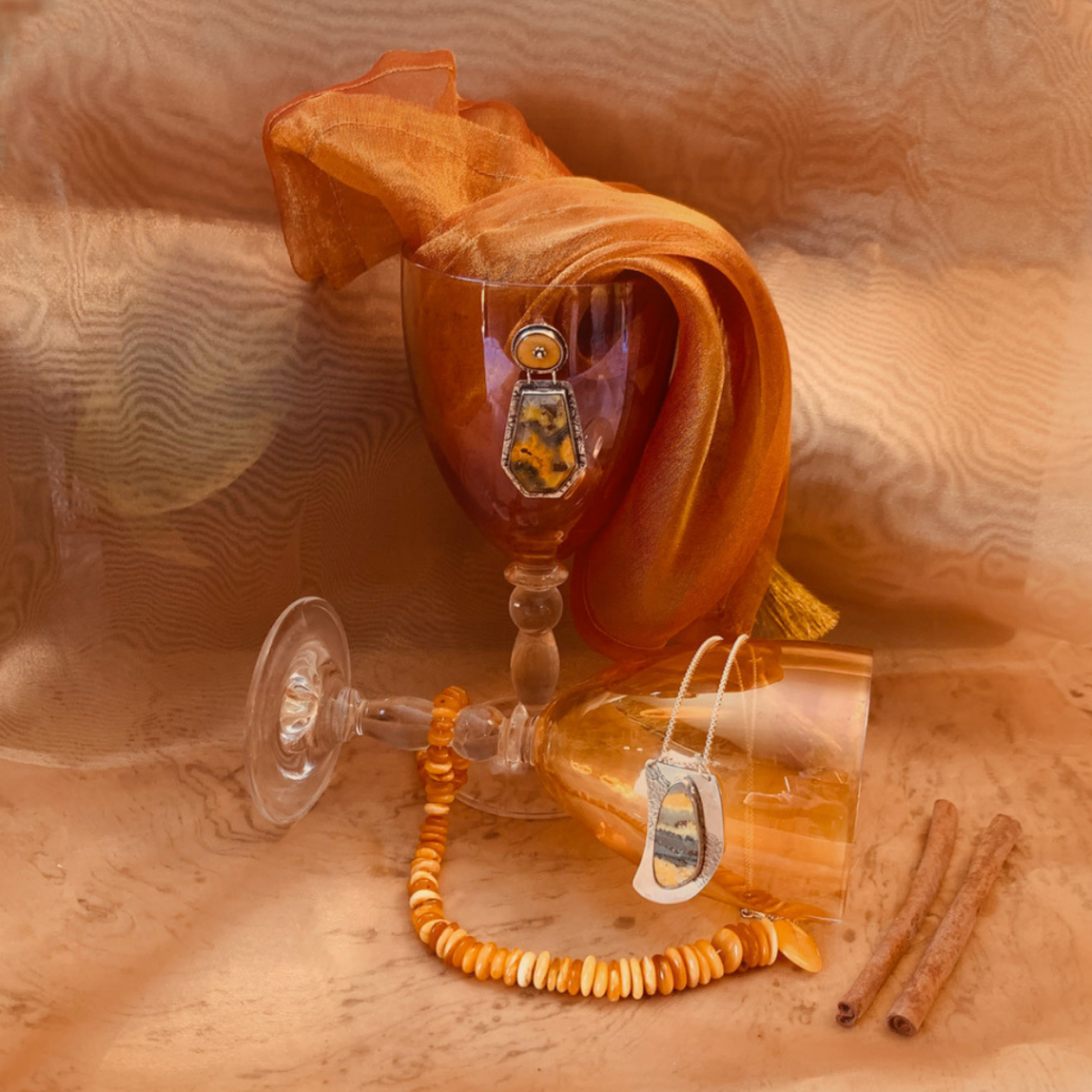 A photograph of orange wine glasses, fabric and jewelry placed on an orange backdrop.