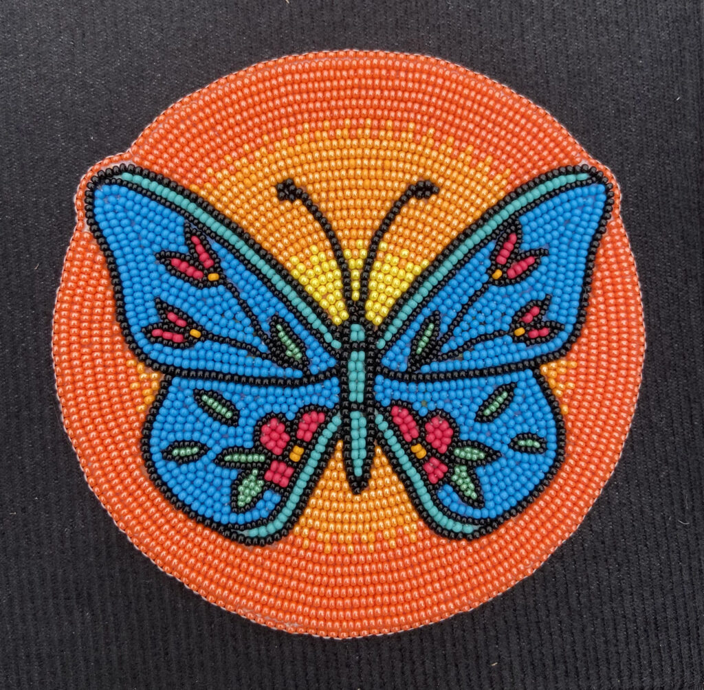 A beaded blue and pink butterfly in front of a yellow to red gradient sky.