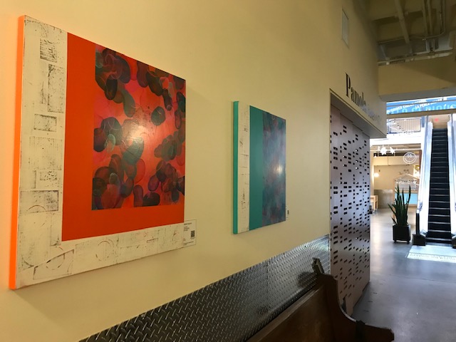 Large abstract prints in red and blue hang on a white wall in River market.