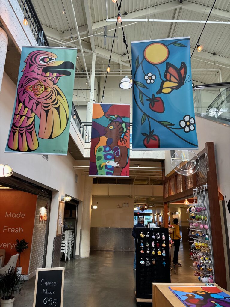 Three multicoloured banners in coast sailish and woodlands art styles hang from the rafters at River Market