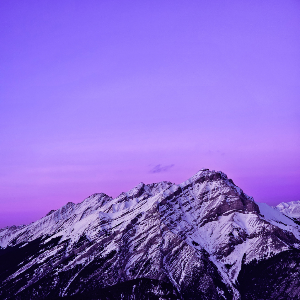 Snow peaked mountain tops stand resolute against a purpling sunset sky.