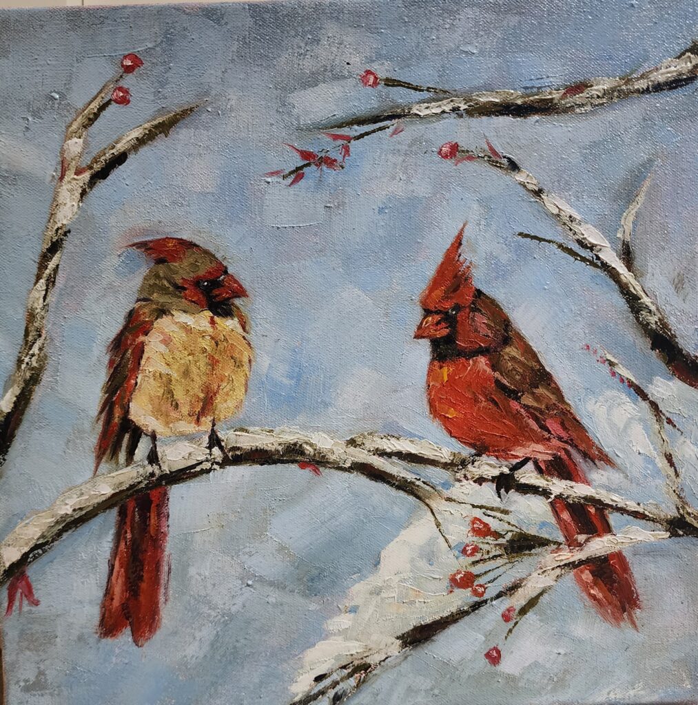 two red birds sit on snow covered branches, red berries and a blue sky behind them