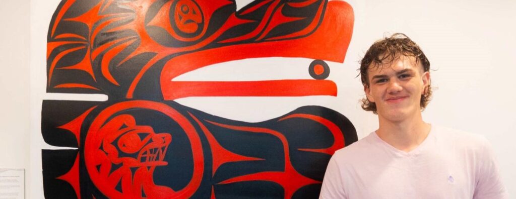 Ryan stands next to a red and black mural painted on a white wall.