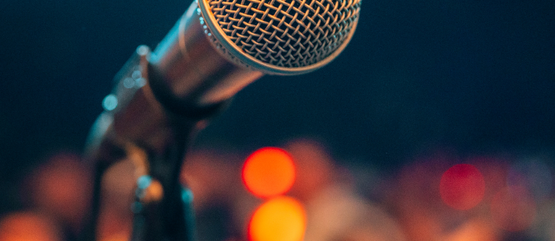 A microphone stands before out of focus orange lights.