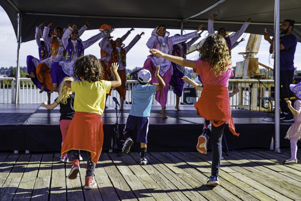 Children dance enthusiastically along with performers on a stage at the New West Quay.