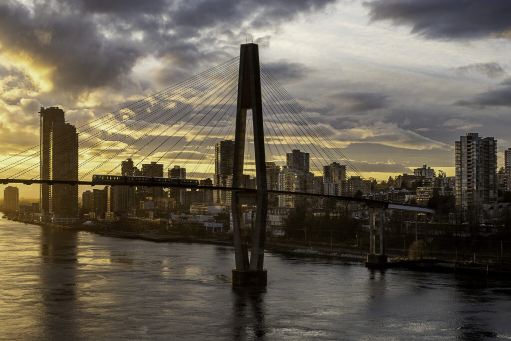 The skytrain bridge stands tall before the skyline of New West along the Fraser River at sunset