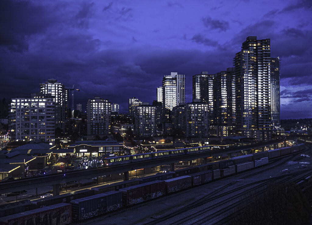 The skyline of downtown New Westminster lit up at night seen from beyond the train yard.