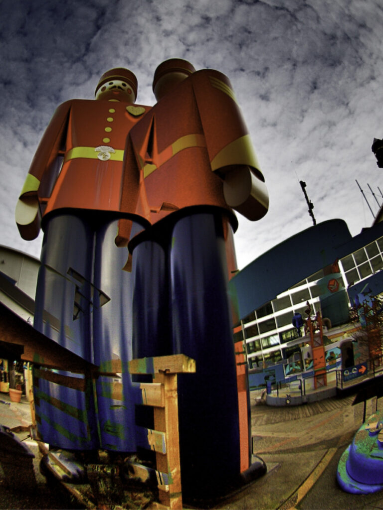 Two large tin soldiers wearing red coats and blue pants rise up in the foreground in front of the Fraser River Discovery Centre