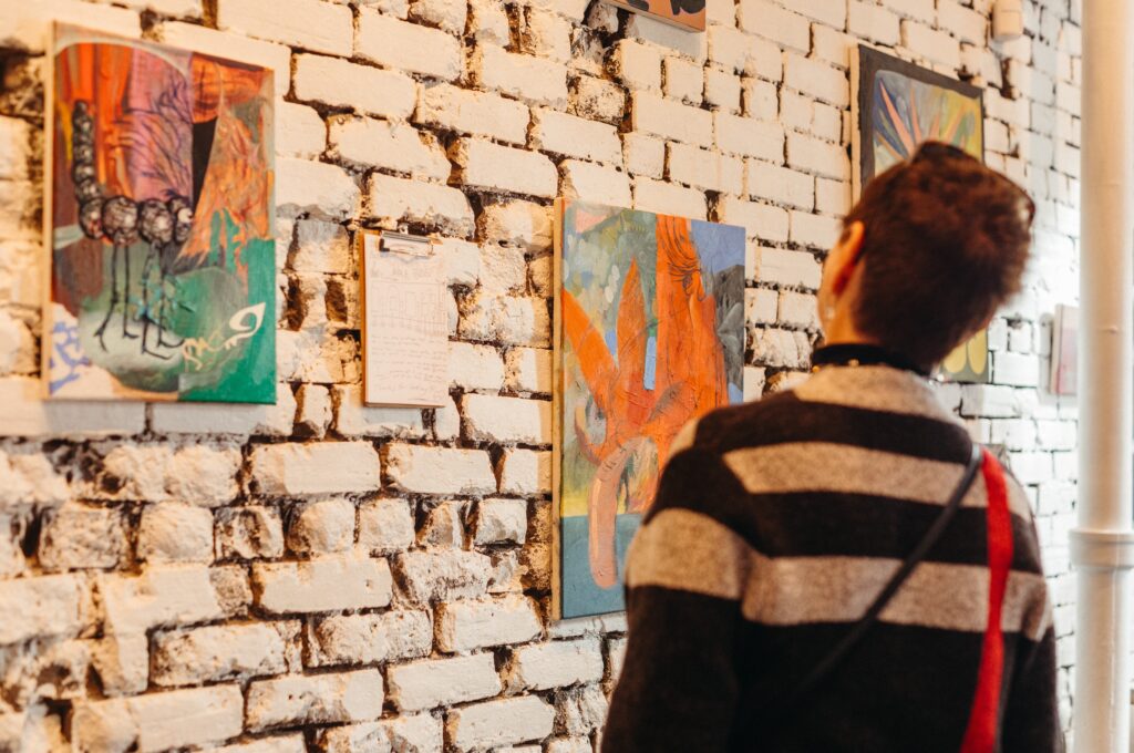 A woman admires multicolour abstract paintings hung on a white brick wall