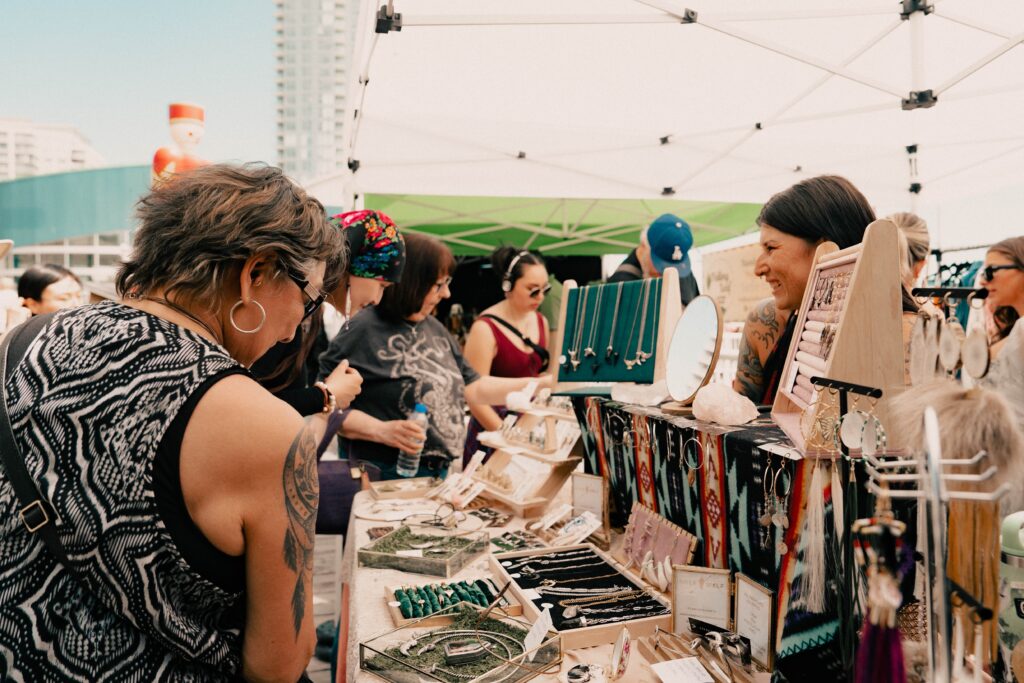 A crowd of people stand around a jewelry stall at New West Craft