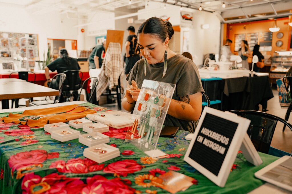 An artisan sits behind their table making beaded jewelry at New West Craft