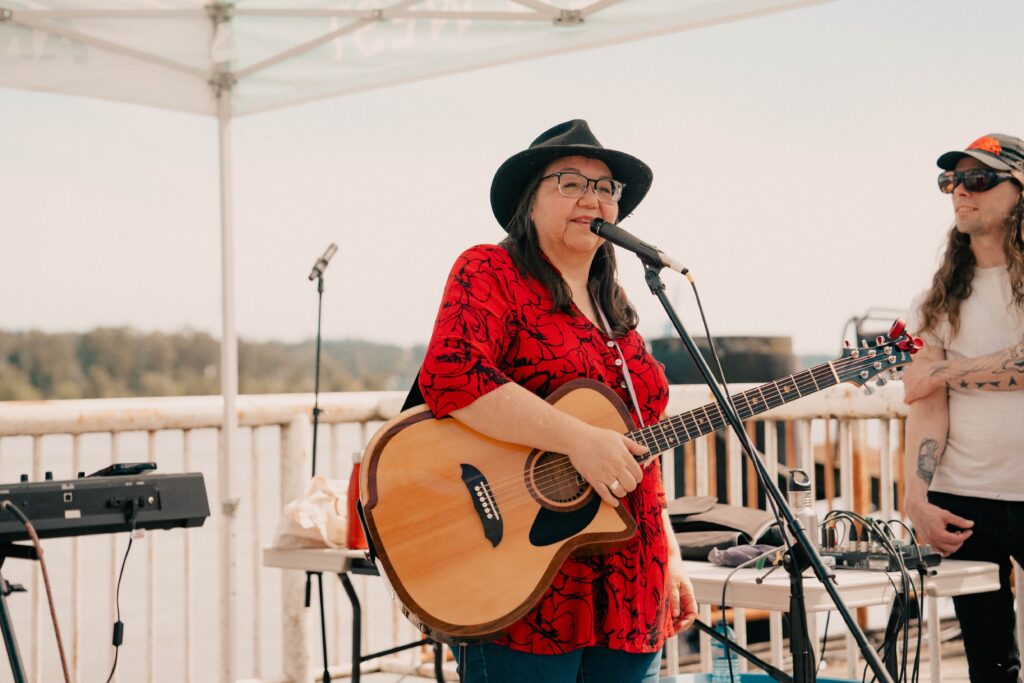 A performer holding a guitar stands behind a microphone