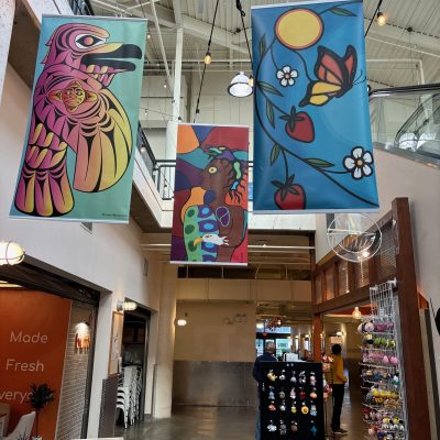 Three multicoloured banners in coast sailish and woodlands art styles hang from the rafters at River Market