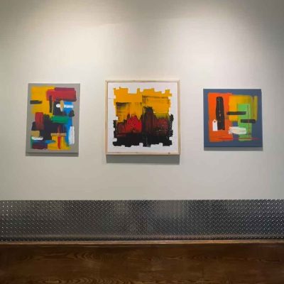 The brightly coloured abstract paintings featuring large block colours hang on a white wall in River Market.